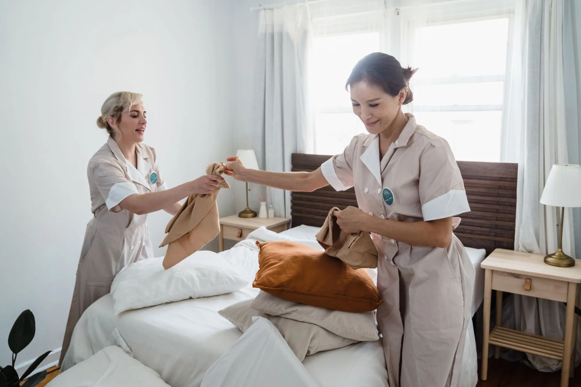 Two uniformed AllStar cleaners making a bed in a bright, tidy bedroom