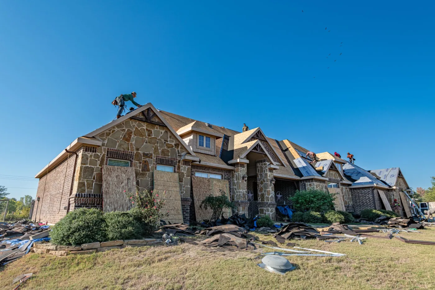 A crew re-roofing a large stone and brick Atlanta home, old shingles cleared off the roof