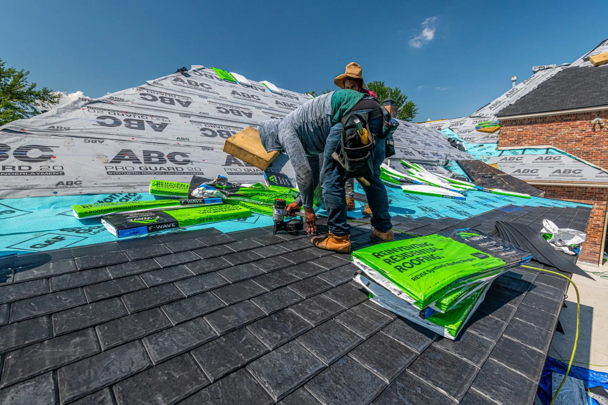 A roofer laying dark shingles on an Atlanta home against a clear blue sky