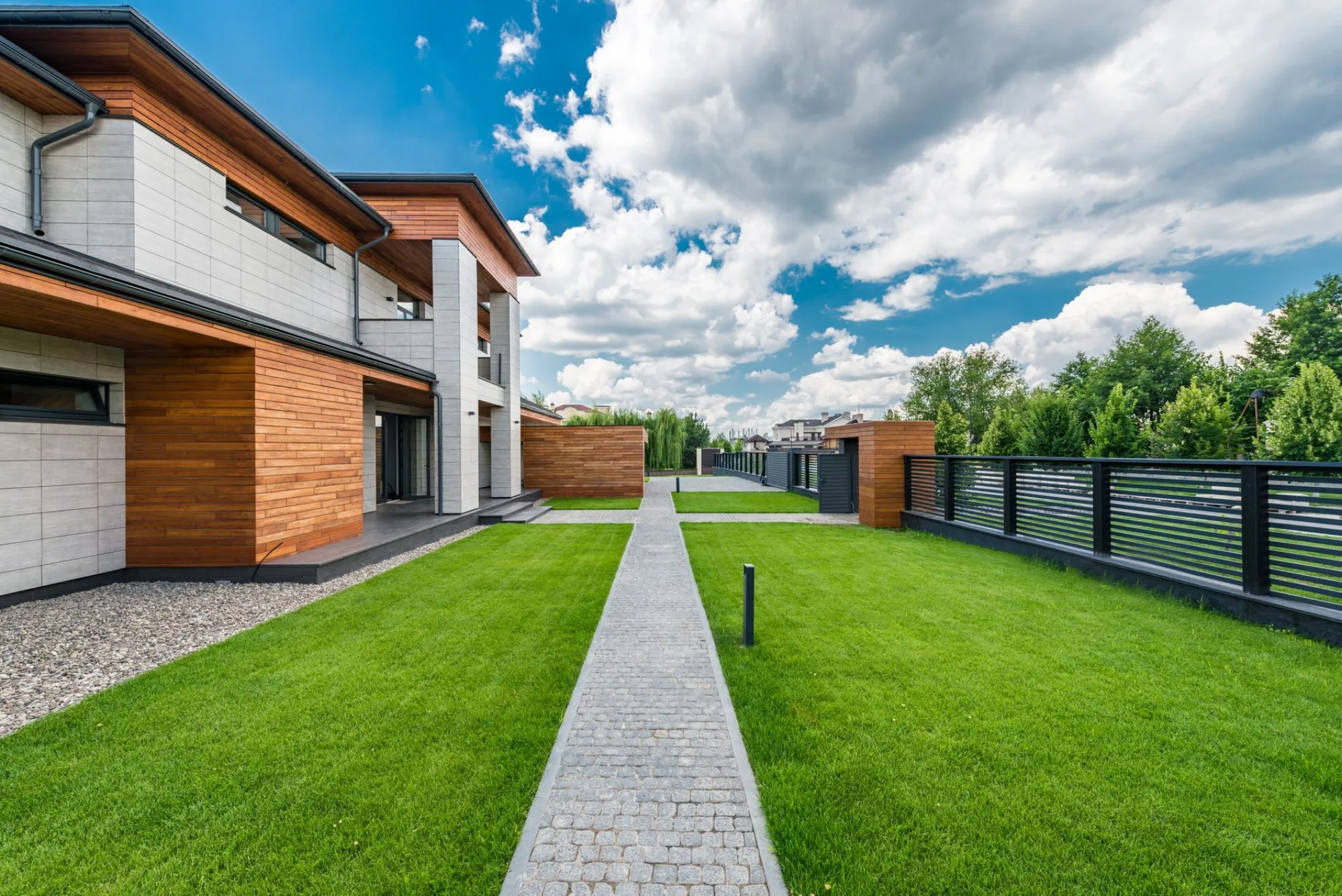 A modern architectural home with a crisp striped green lawn and a clean walkway under a blue sky