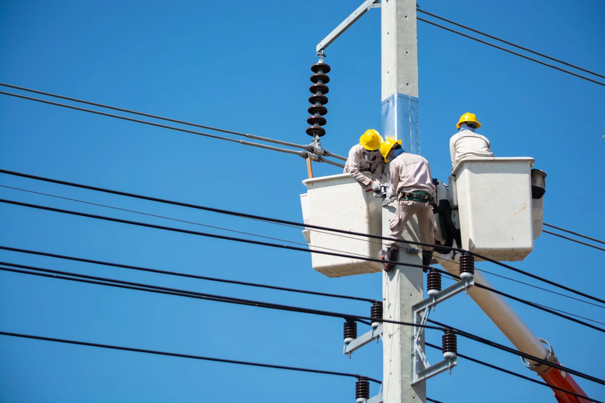 Two Cleveland Electric line workers up on a power pole against a clear blue sky