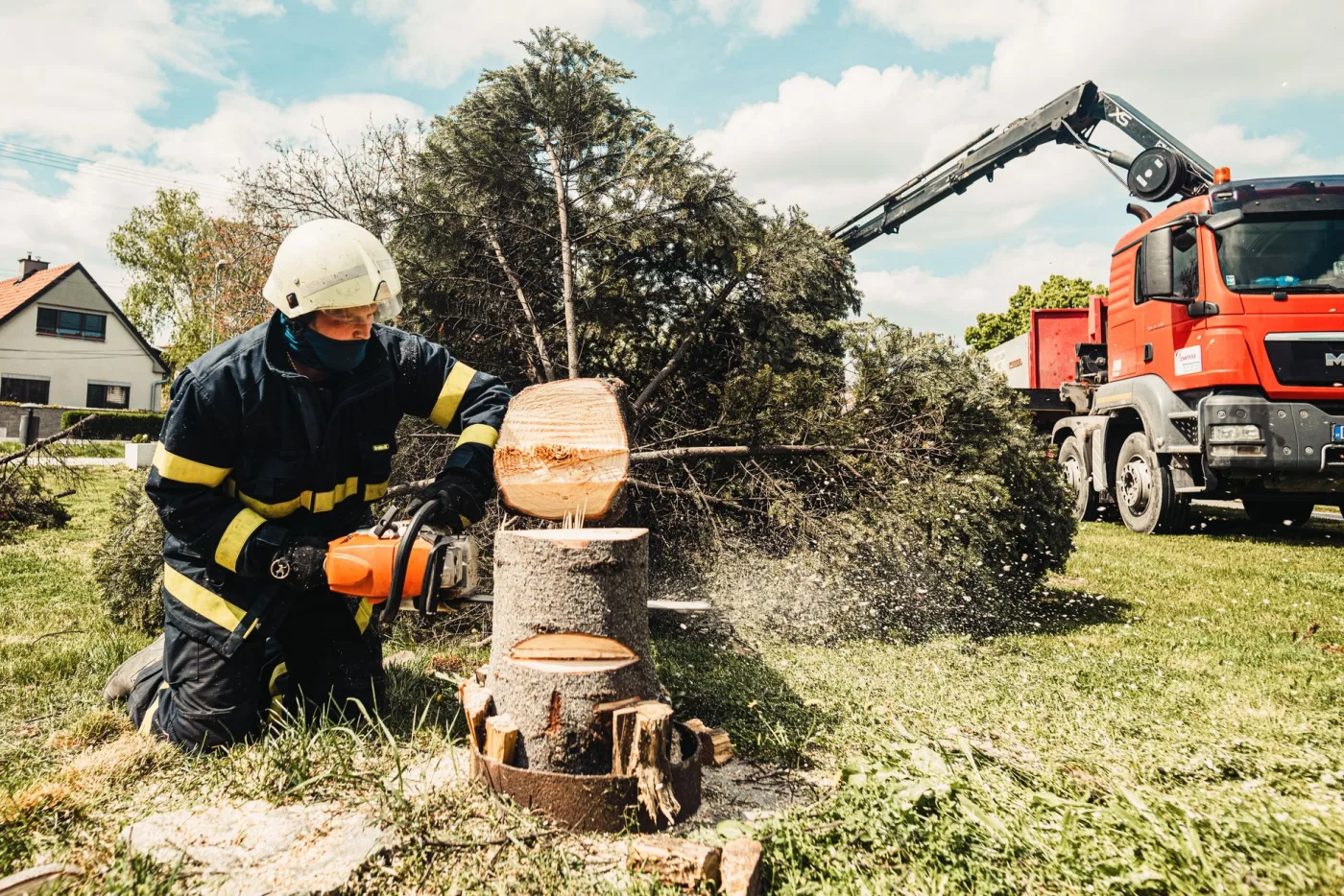 A Diamond crew member cutting a large stump with a truck and crane behind