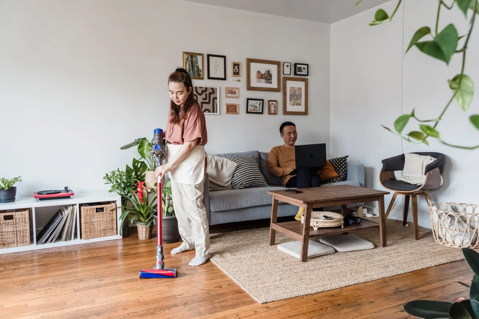 A person tidying a warm, plant-filled living room