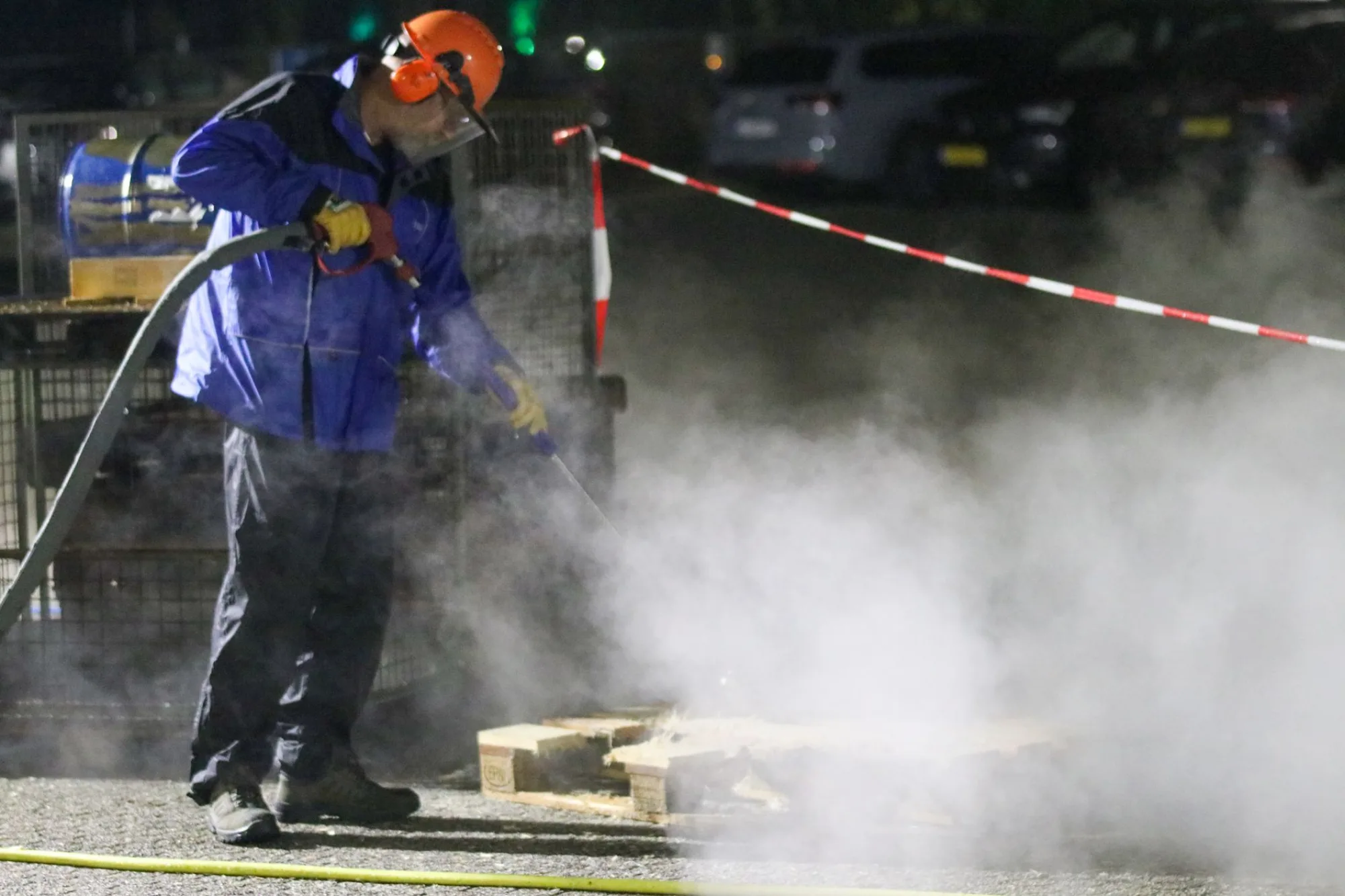 A technician pressure washing pavement with a wide fan of water and rising steam