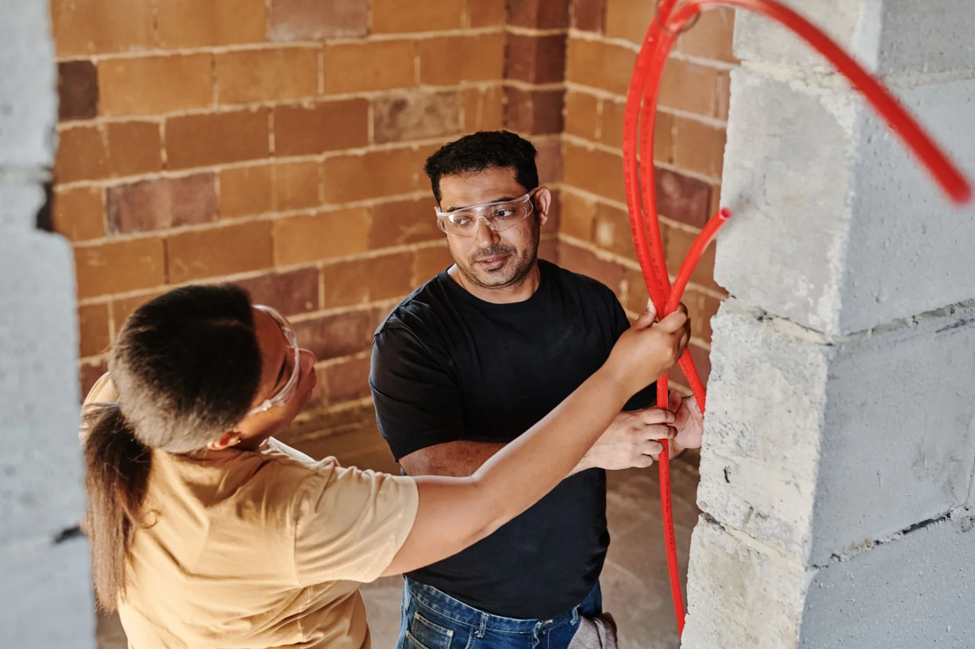 Two electricians running a bright cable along a wall