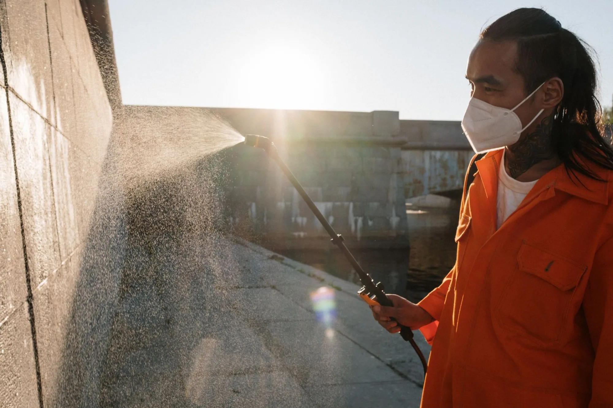 A pressure washing technician spraying a wall in bright backlit sun