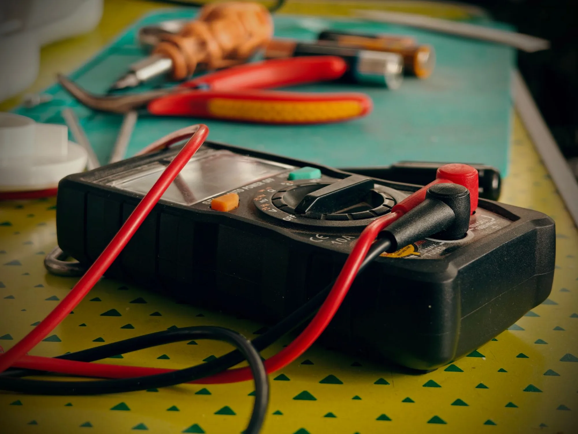 Multimeter and hand tools with red test leads on an electrician's workbench