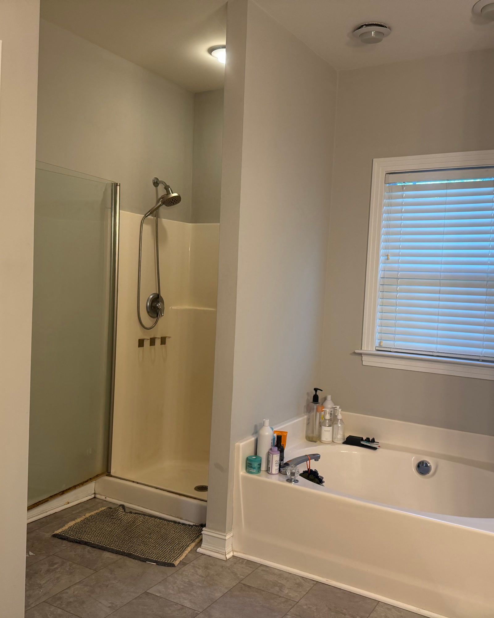 Before: the master bathroom with a yellowed fibreglass shower surround, a dated tile floor, a builder grade tub and a single glass panel.