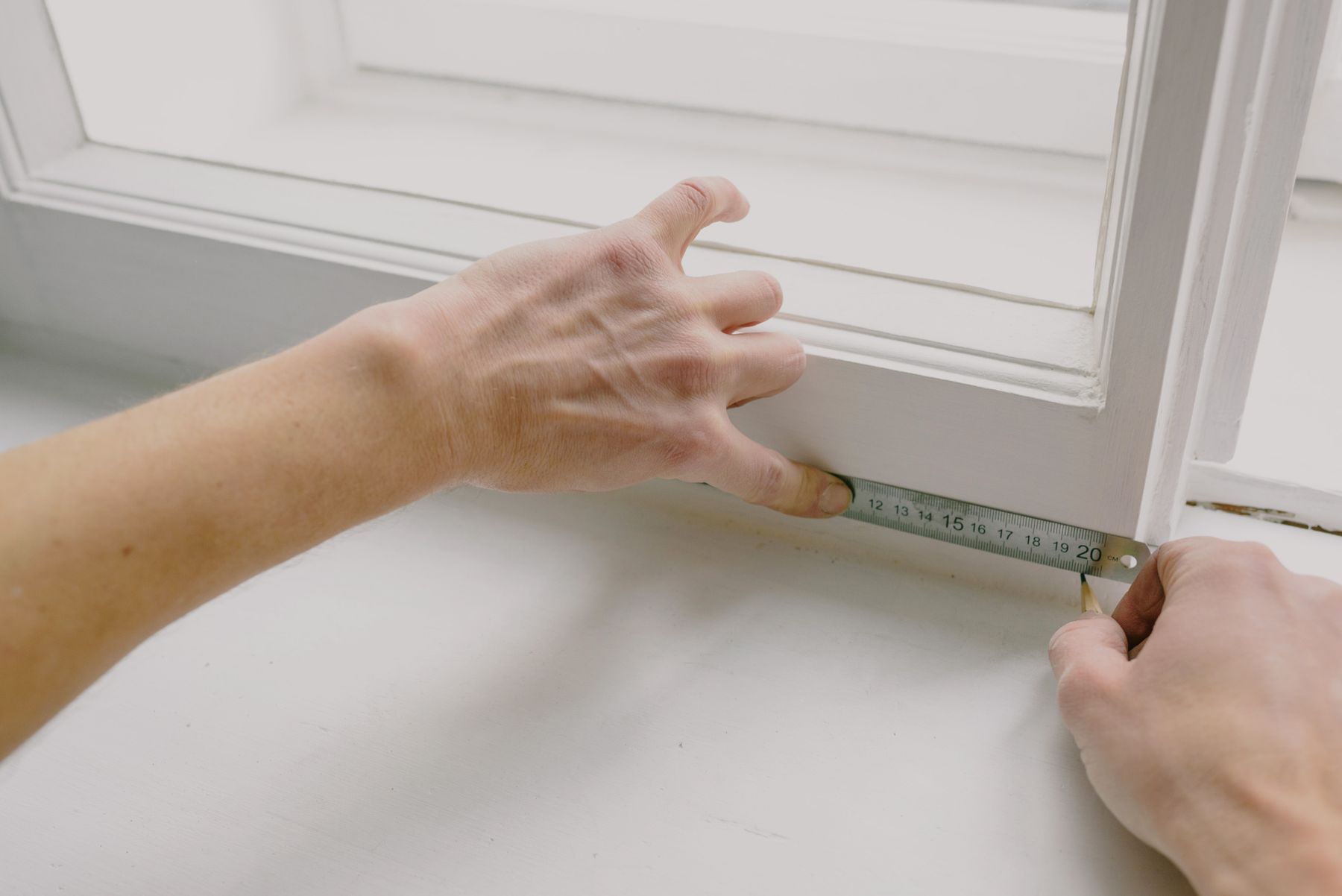 A pair of hands measuring a painted window frame with a folding rule.