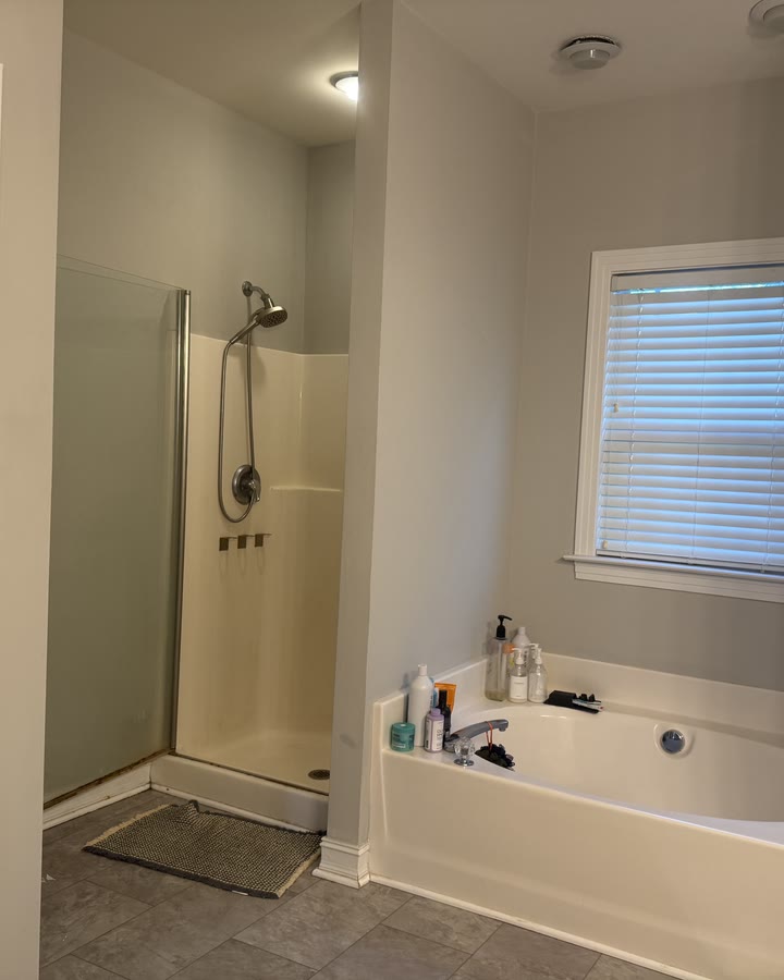 The same corner before the remodel: a dated fiberglass shower insert with a framed glass door beside the garden tub.