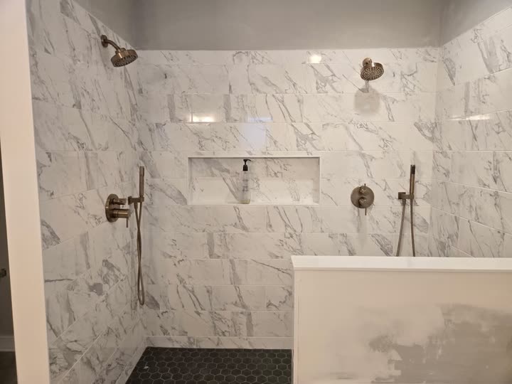 The finished shower wall: marble-look tile to the ceiling, two shower heads, a recessed niche and brushed nickel valves.