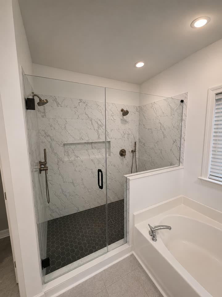 The finished shower with the frameless glass door hung, black hex mosaic floor and the tub alongside.