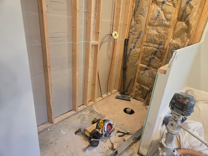 The shower opened back to the studs, with the new drain set in the subfloor and a laser line marking the tile height.