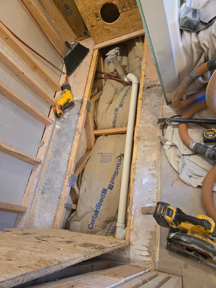 The floor opened up for the new drain line, showing the plumbing stack and the insulation behind it.