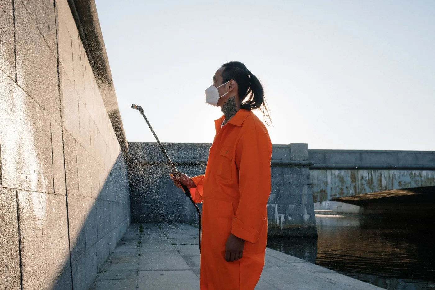 A technician soft-washing a stone masonry wall with a low-pressure wand