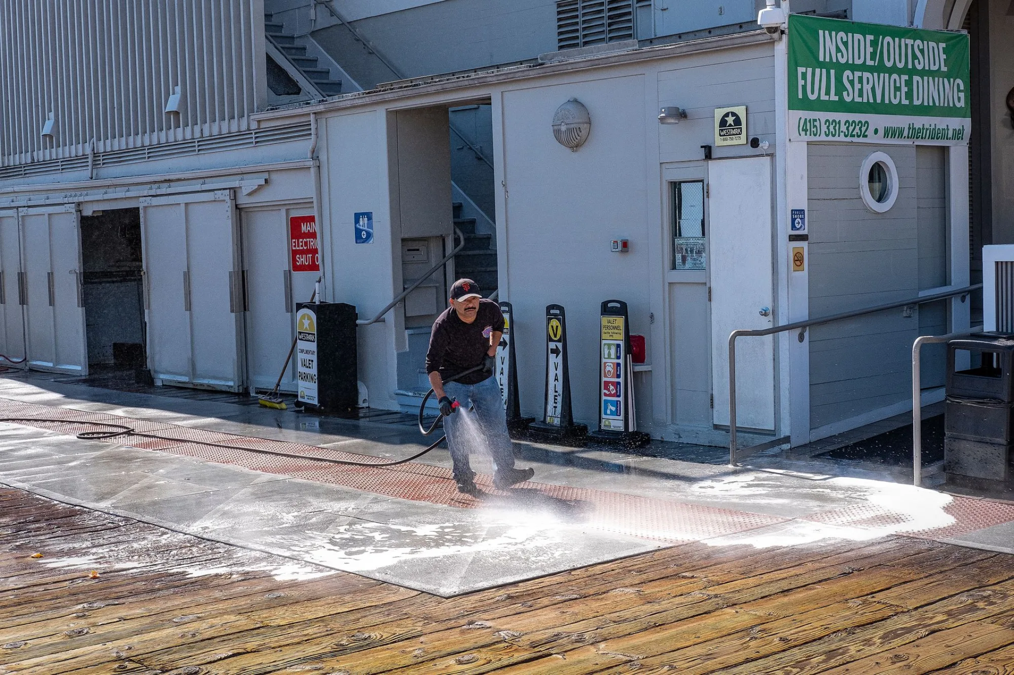 A worker pressure washing a walkway, water spray and foam lifting grime off the surface